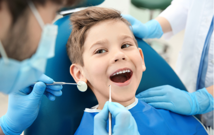 Boy at dentist office having routing dental exam with a big smile to show off teeth