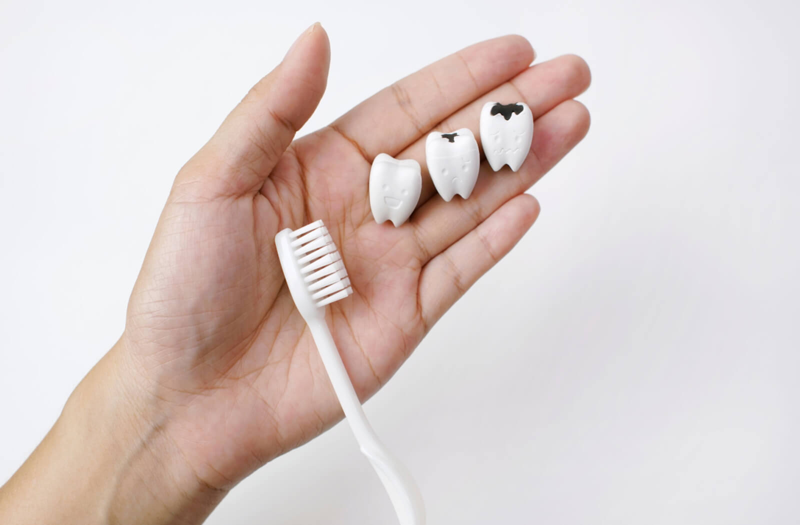 a hand holds three fake teeth with varying degrees of tooth decay