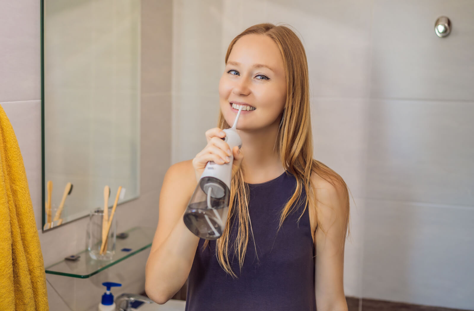Young woman in her bathroom using her Waterpik to clean her teeth.