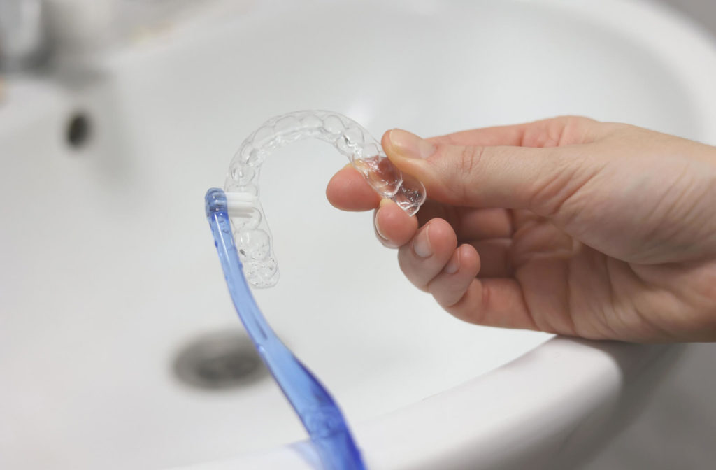 close-up of a hand holding an Invisalign tray and cleaning it using a soft bristle toothbrush.